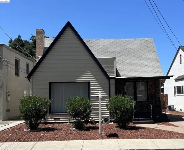 A-frame gable roofline, light-colored siding, covered entry with stone-finish exterior, front yard with decorative ground cover, and sidewalk access