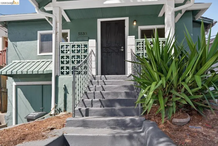 Stucco exterior with a covered porch featuring decorative concrete block railings and dark wrought iron handrails