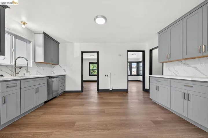 Kitchen featuring wood-finish flooring, two-tone cabinetry, stainless steel appliances, and a white countertop with a matching backsplash