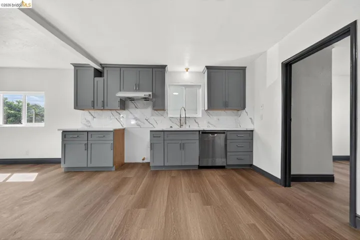 Kitchen featuring gray shaker-style cabinetry, white countertops, marble-patterned backsplash, stainless steel dishwasher, and wood-finish flooring