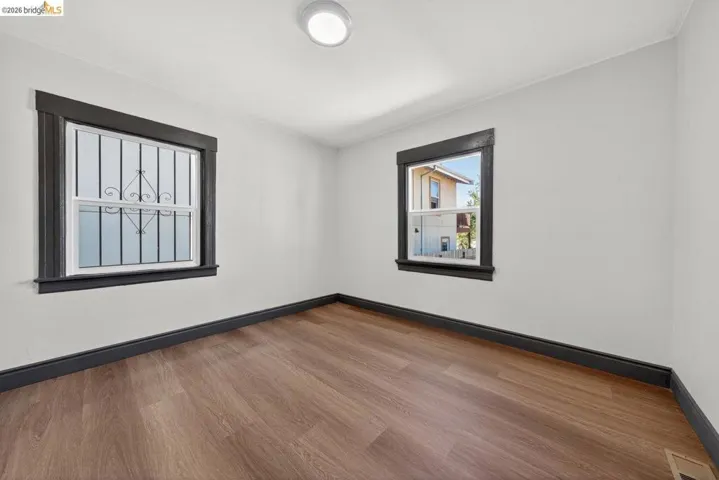 Room featuring light-toned walls, wood-finish flooring, dark trim, and two windows