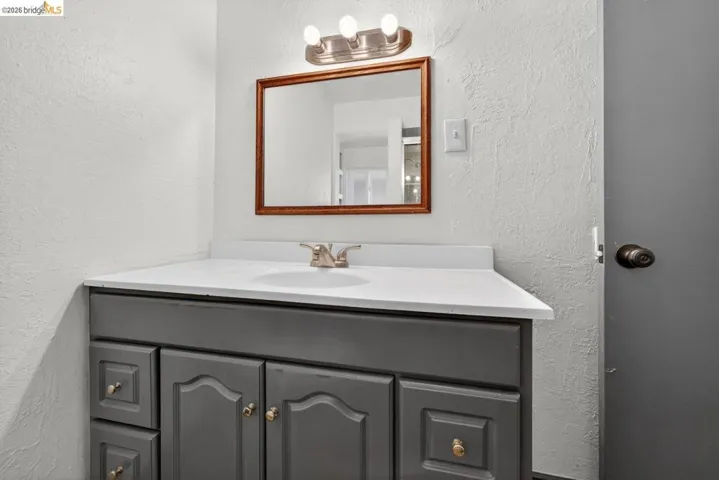 Vanity featuring a dark gray cabinet with gold-toned hardware, an integrated white sink, and a light-toned countertop