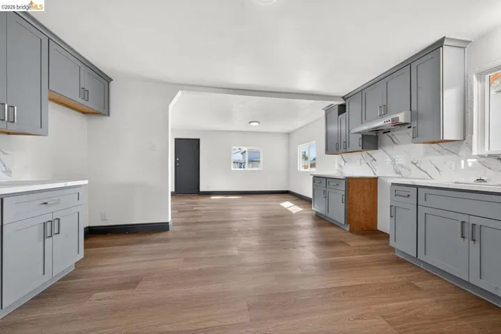 Updated kitchen featuring wood-finish flooring, light gray cabinetry, white countertops, and a white marble-look backsplash