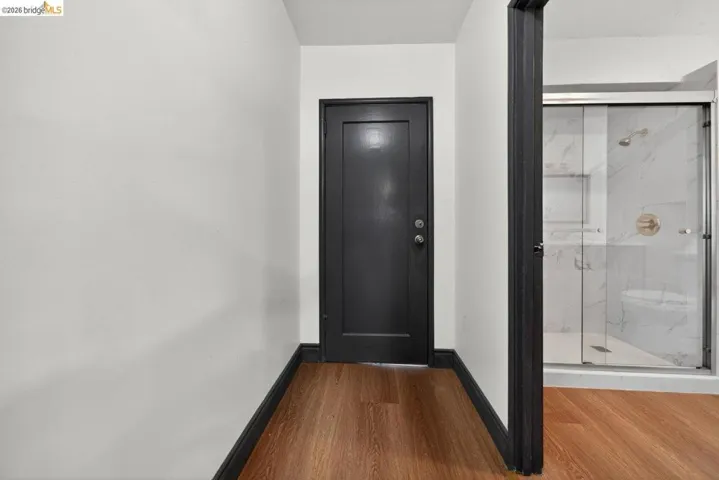 Wood-finish flooring throughout, featuring a dark-paneled door and contrasting white walls