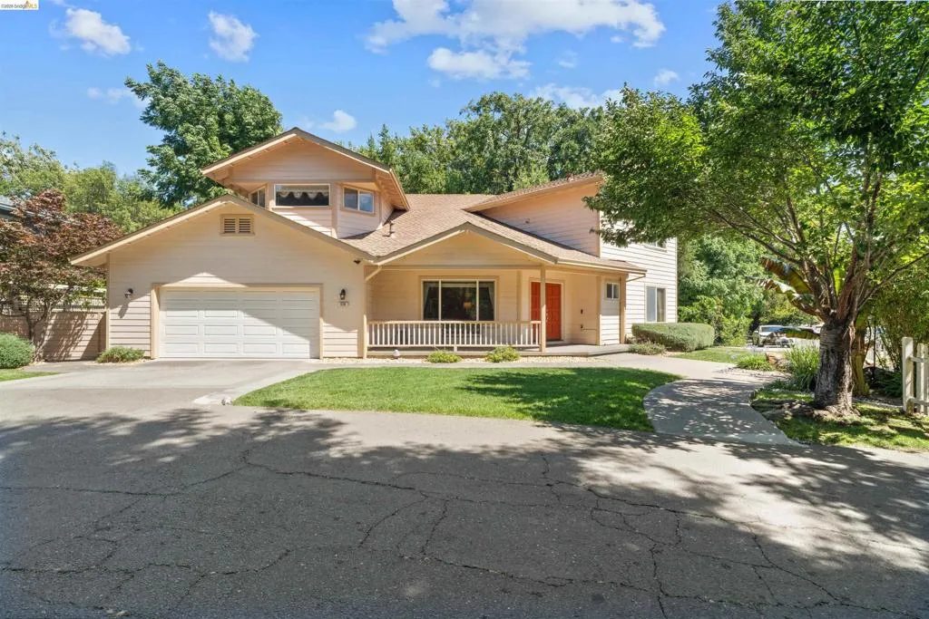 Light-toned multi-level residence featuring a covered front porch with white railing, an attached two-car garage, and a distinct orange entry door