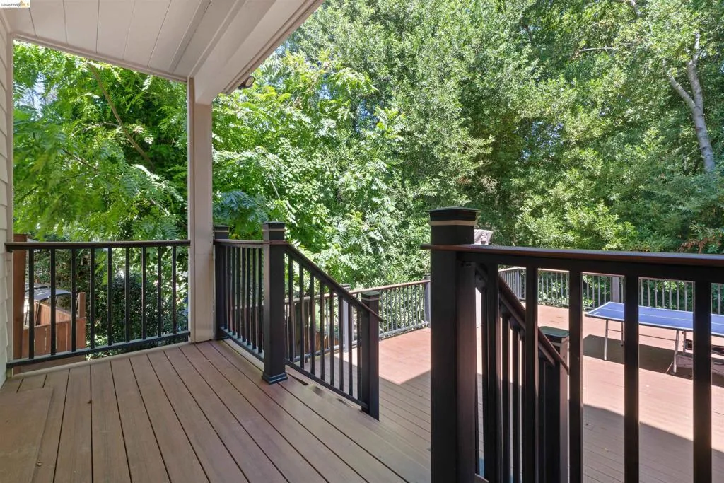 Spacious outdoor deck featuring composite wood-finish flooring, dark metal railings, and a covered porch area