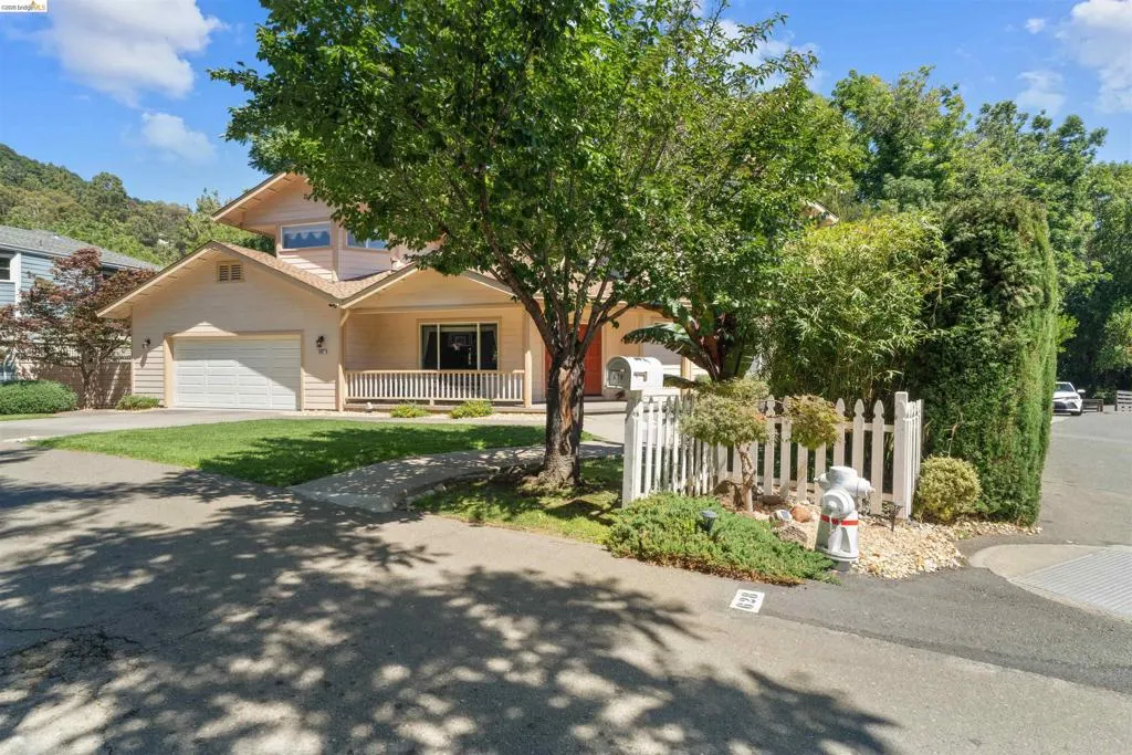 Two-story residence featuring a front porch with white railing, an integrated garage, and multiple mature trees