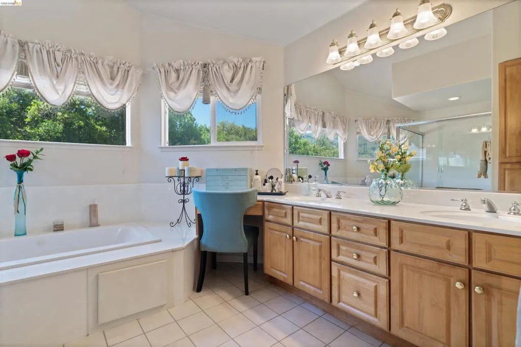 Dual vanities with integrated sinks, ample wood cabinetry, a built-in soaking tub, and tile flooring