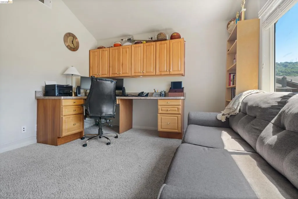 Integrated built-in desk with overhead cabinetry, light-colored carpeting, a large window, a built-in bookshelf, and sloped ceilings