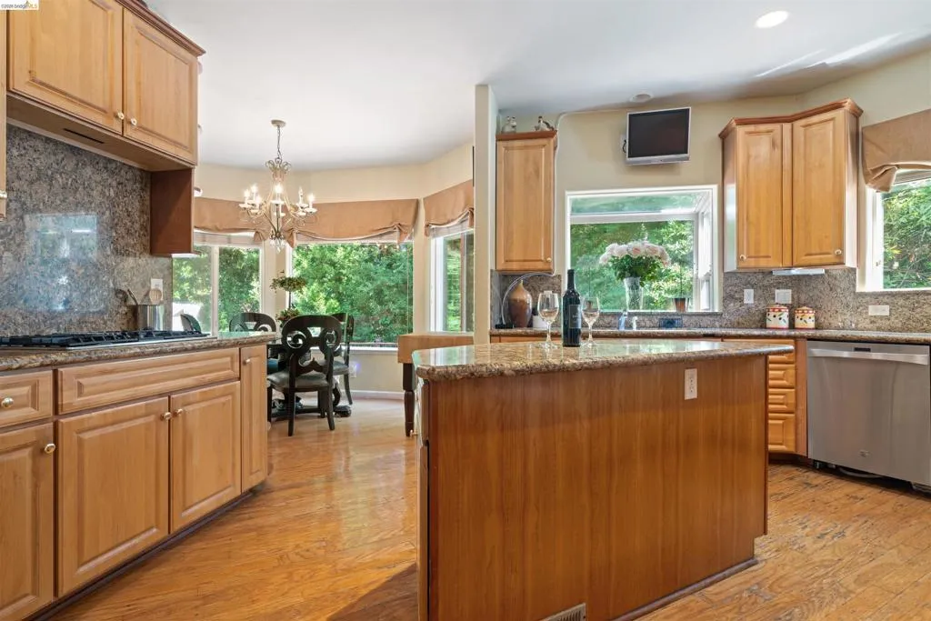 Kitchen featuring wood cabinetry, granite countertops, a central island, wood-finish flooring, and a stainless steel dishwasher
