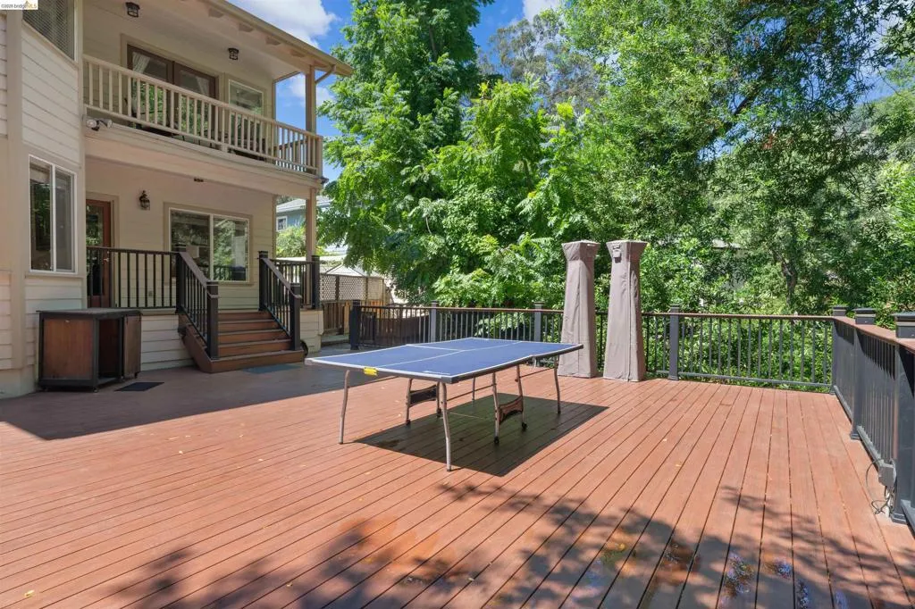 Expansive wood-finish deck featuring dark railings, a lower-level entry, and a covered upper-level balcony