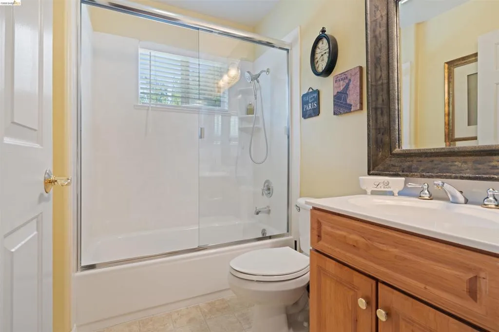 Bathroom featuring a built-in tub with a sliding glass enclosure, white vanity with an integrated sink, wood-finish cabinetry, and chrome fixtures