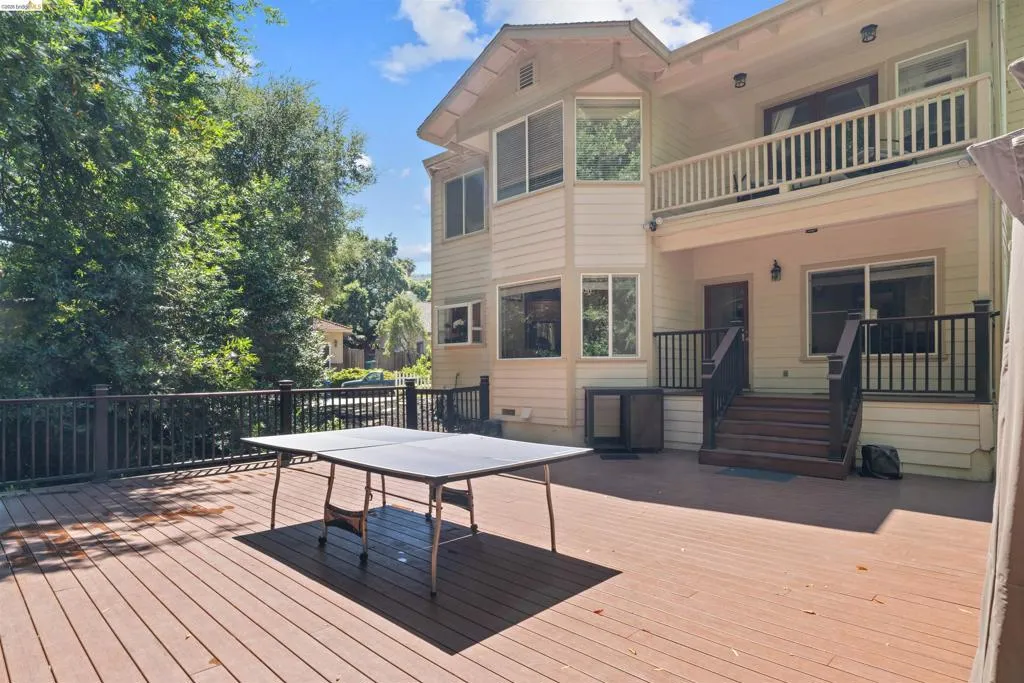 Multi-level wood-finish deck with dark railings and steps, featuring a light-colored exterior with multiple windows and an upper-level balcony