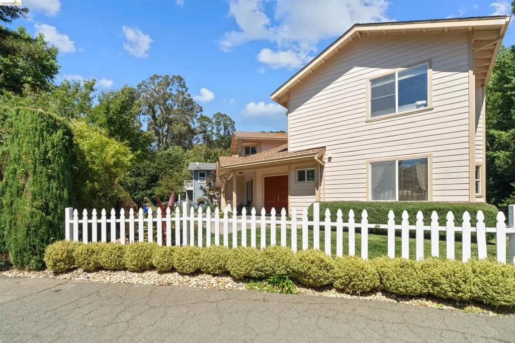 Two-story residence featuring light-colored siding, a white picket fence, and mature green landscaping