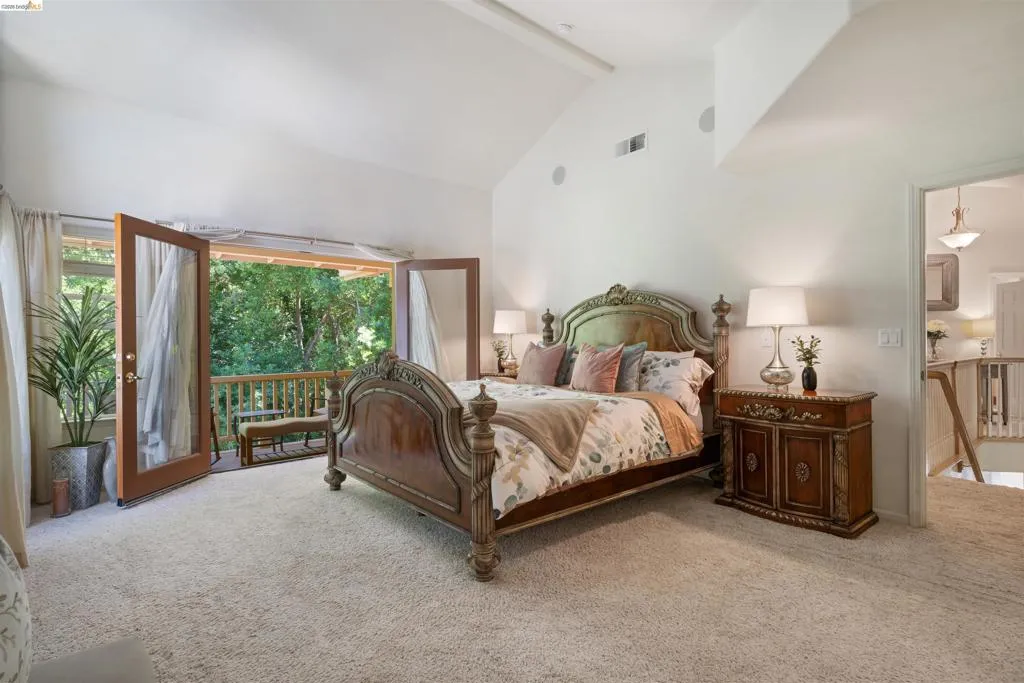 Carpeted bedroom featuring vaulted ceilings and double French doors opening to a private balcony