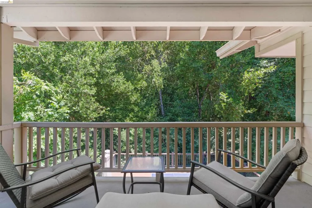 Covered balcony with a wooden balustrade, featuring a verdant tree canopy backdrop