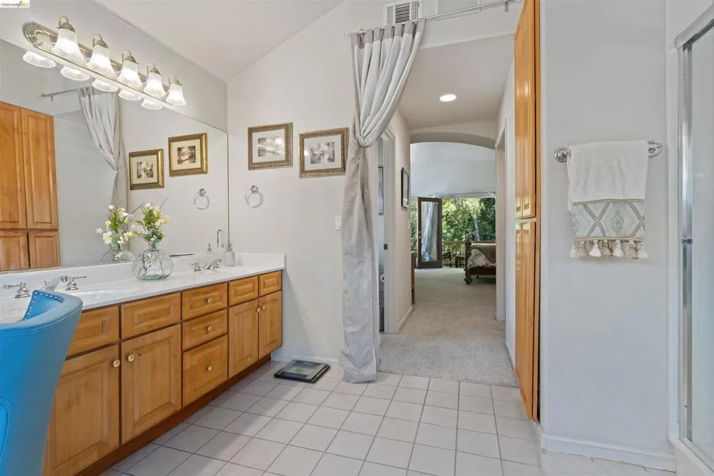 Bathroom featuring a light-toned wood double vanity with white countertops, dual sinks, and a large wall mirror with multi-bulb vanity lighting