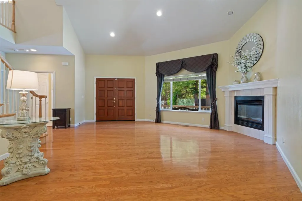 Spacious interior featuring wood-finish flooring, a double-door entry, a prominent fireplace with a white mantel, high ceilings, and abundant natural light from a large window