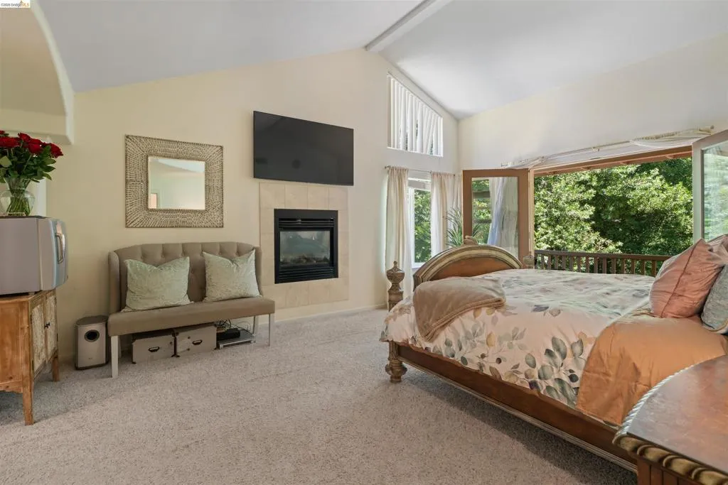 Carpeted interior featuring a fireplace with a light-toned tile surround, vaulted ceiling, and multiple windows
