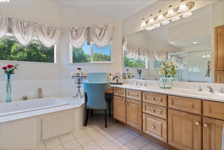 Dual vanities with integrated sinks, ample wood cabinetry, a built-in soaking tub, and tile flooring