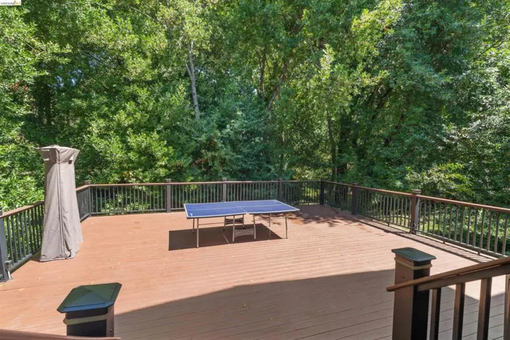 Expansive outdoor deck featuring wood-finish flooring and dark railings, surrounded by mature trees