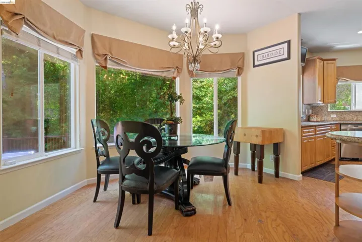 Dining area with light wood-finish flooring and multiple windows featuring neutral-toned fabric valances