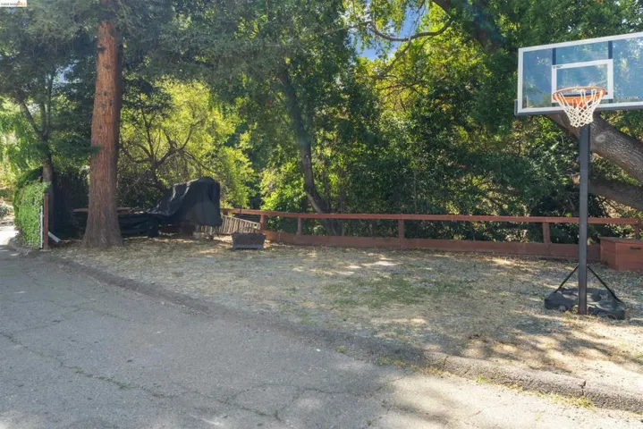 Paved driveway with a partial wooden fence and mature trees