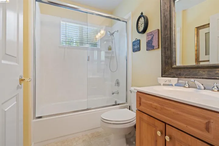 Bathroom featuring a built-in tub with a sliding glass enclosure, white vanity with an integrated sink, wood-finish cabinetry, and chrome fixtures