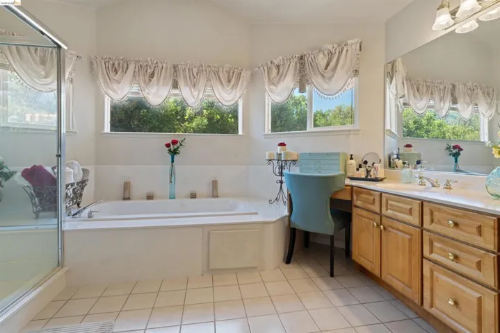 Bathroom featuring a built-in tub, separate glass-enclosed shower, wood-finish vanity with countertop, a large wall-mounted mirror, and tile flooring