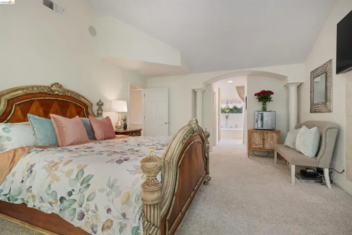 Spacious room featuring vaulted ceilings, neutral carpeting, and an arched entry to a bathroom with a built-in tub