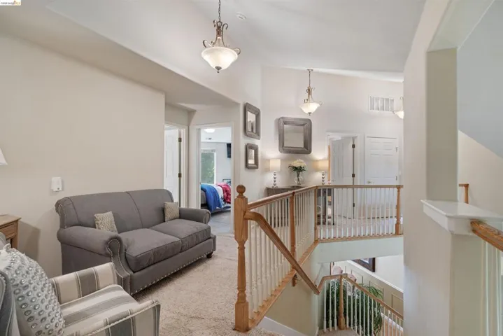 Multi-level interior featuring vaulted ceilings, light-tone wall paint, a carpeted hallway, and a wood railing with white balusters
