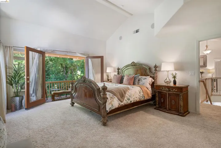 Carpeted bedroom featuring vaulted ceilings and double French doors opening to a private balcony