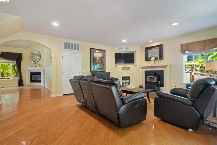 Spacious room featuring wood-finish flooring, recessed lighting, and a prominent fireplace with a stone-finish surround
