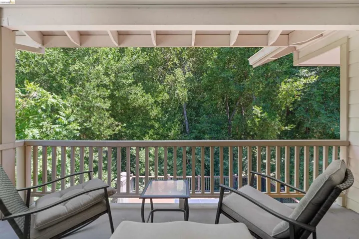 Covered balcony with a wooden balustrade, featuring a verdant tree canopy backdrop