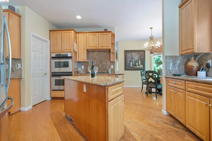 Kitchen featuring natural wood cabinetry, granite countertops, wood-finish flooring, a central island, and double wall ovens