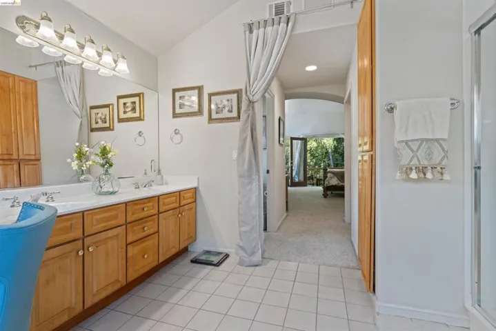 Bathroom featuring a light-toned wood double vanity with white countertops, dual sinks, and a large wall mirror with multi-bulb vanity lighting