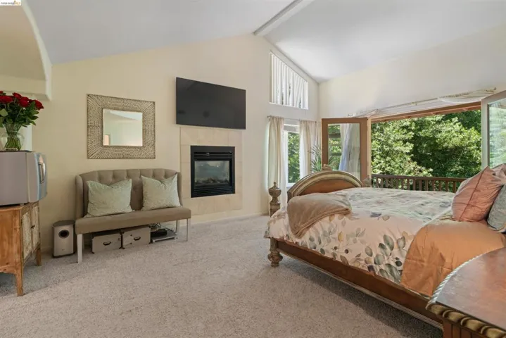 Carpeted interior featuring a fireplace with a light-toned tile surround, vaulted ceiling, and multiple windows