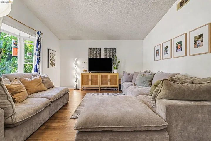 Living area featuring wood-finish flooring, vaulted ceiling, and recessed bay window