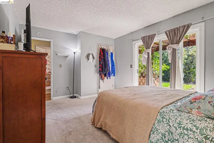 Sliding glass doors opening to outdoor space, light gray walls, textured ceiling, light-colored carpeting, and a built-in closet