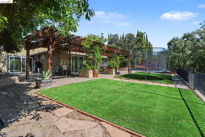 Expansive outdoor living area featuring a wood pergola, artificial turf lawn, flagstone patio, and mature landscaping