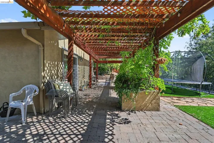 Expansive outdoor patio featuring a wooden pergola with integrated string lighting, brick paver flooring, and lush greenery