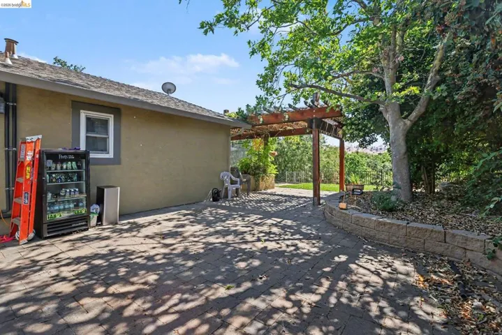 Paver patio with a wood pergola, bordered by a stone retaining wall and mature trees