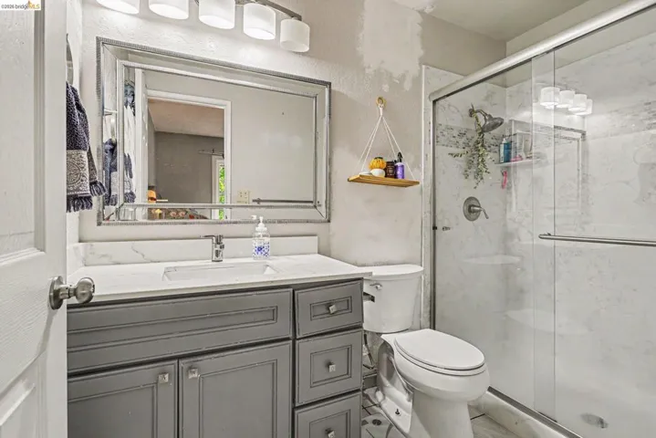 Bathroom featuring a grey wood-finish vanity with square hardware, white countertop with an integrated sink, and a framed mirror