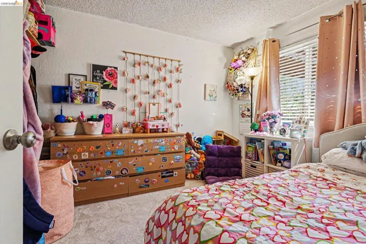 Carpeted room featuring a window with blinds and drapes, a built-in shelving unit, and a dresser
