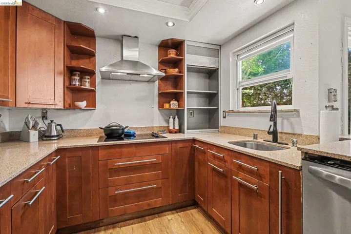Kitchen featuring wood cabinetry, light-toned countertops, stainless steel appliances, a built-in cooktop, and an undermount sink with a dark-finish faucet