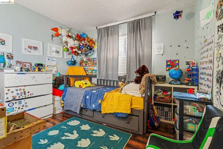 Bedroom featuring wood-finish flooring, light blue wall paint, and window with blinds