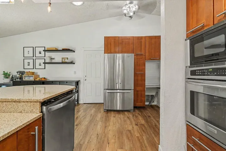 Kitchen featuring wood-finish flooring, stainless steel appliances, wood cabinetry, and a vaulted ceiling