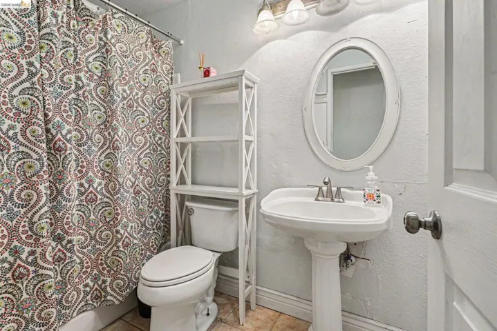 Bathroom featuring a white pedestal sink with brushed nickel faucet, an oval wall-mounted mirror, and a wall-mounted light fixture with three sconces