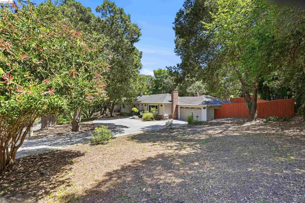 Ranch-style residence featuring a prominent brick chimney, an attached two-car garage, and a terracotta-toned privacy fence