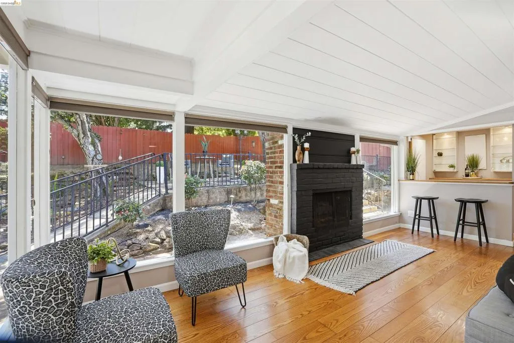 Living area featuring expansive windows, wood-finish flooring, a painted brick fireplace, a built-in bar with display cabinetry, and a slatted white ceiling